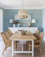 A coastal dining room featuring a light oak modern dining table, vintage rattan chairs, a distressed white buffet, and a contemporary capiz shell chandelier, with walls painted in a soft Palladian Blue. — styling and décor detail