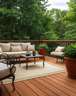 A traditional deck featuring warm-toned cedar decking and railings, wrought iron furniture with cream cushions, an outdoor rug in a natural beige, and terracotta planters filled with green foliage, all under soft, natural light. — close-up of textures and materials