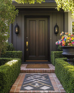 A traditional front yard featuring a dark wood front door with brass hardware, flanked by symmetrical boxwood hedges and modern matte black sconces. A reclaimed brick pathway leads to the entrance, with a vintage cast iron urn holding colorful flowers and a sleek geometric doormat. — alternate angle