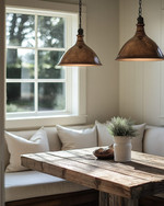 A warm and inviting farmhouse breakfast nook featuring a rustic reclaimed wood table, a cream banquette with linen cushions, and two aged bronze pendant lights hanging over the table, with soft morning light streaming through a window.