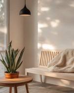 A Scandinavian porch featuring a light ash slatted bench with a cream knit throw, a small round teak coffee table, and a sculptural snake plant in a terracotta pot, all under the soft glow of a matte black outdoor pendant light. — alternate angle