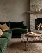 A Rustic Landscape living room featuring a deep forest green velvet sofa, a reclaimed wood coffee table, and a rough-hewn stone fireplace. Natural light illuminates the warm greige walls, complemented by woven jute rugs and subtle ochre throw pillows. — styling and décor detail
