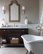 Traditional bathroom featuring a white clawfoot tub, a dark wood console vanity with a Carrara marble top, polished nickel fixtures, and an ornate gilded mirror above the sink, all under warm sconce lighting. — styling and décor detail