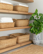 Cozy boho laundry room featuring light oak floating shelves, natural rattan laundry baskets, a woven jute rug, and a ceramic planter with a lush Pothos plant, all under soft, warm lighting. — close-up of textures and materials