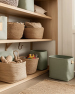 Boho closet storage with open mango wood shelving, large woven rattan baskets for toys, and canvas bins in muted sage green. A low-pile jute rug sits on the floor, and a small, dedicated hook is placed at a child's height. — styling and décor detail