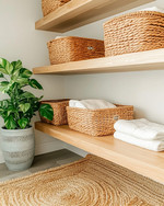 Cozy boho laundry room featuring light oak floating shelves, natural rattan laundry baskets, a woven jute rug, and a ceramic planter with a lush Pothos plant, all under soft, warm lighting. — styling and décor detail