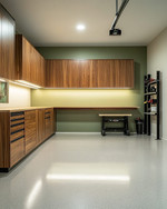 Clean Mid-Century Modern garage featuring walnut flat-panel cabinetry, a polished light grey epoxy floor, recessed LED lighting, and a subtle sage green accent wall behind a minimalist workbench. — styling and décor detail