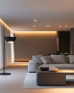 A modern living room at dusk with layered lighting, featuring recessed ceiling lights, a sleek matte black floor lamp beside a light gray sofa, and a sculptural pendant light illuminating a minimalist coffee table. Warm white light creates an inviting ambiance.