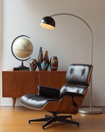 A sophisticated Mid-Century Modern library featuring an Eames Lounge Chair in black leather and walnut, an Arco floor lamp arching over, and a teak credenza displaying abstract ceramic vases and a vintage globe, all under the warm glow of a Sputnik chandelier. — close-up of textures and materials