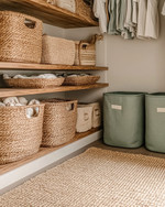 Boho closet storage with open mango wood shelving, large woven rattan baskets for toys, and canvas bins in muted sage green. A low-pile jute rug sits on the floor, and a small, dedicated hook is placed at a child's height. — close-up of textures and materials