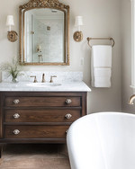 Traditional bathroom featuring a white clawfoot tub, a dark wood console vanity with a Carrara marble top, polished nickel fixtures, and an ornate gilded mirror above the sink, all under warm sconce lighting.