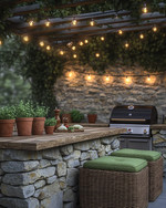 A cozy rustic outdoor kitchen featuring a stacked stone island with a natural wood countertop, a built-in grill, and string lights draped overhead. Terracotta pots with herbs sit on the counter, and comfortable wicker stools with green cushions are pulled up to the bar. — close-up of textures and materials