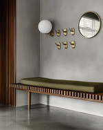 A Mid-Century Modern mudroom featuring a walnut slatted bench, polished concrete flooring, and an olive green upholstered cushion. Brass hooks line the wall above, with a circular mirror and a small white globe sconce adding modern accents. — close-up of textures and materials