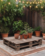 A budget-friendly Boho Backyard featuring a low wooden pallet coffee table, layered vintage rugs in muted terracotta and beige, and an assortment of potted green plants in upcycled terra cotta and ceramic containers, all illuminated by warm solar string lights strung overhead. — styling and décor detail