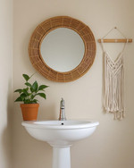 A cozy boho powder room featuring a round rattan mirror above a white pedestal sink, a small Pothos plant in a terracotta pot, and a macrame wall hanging on a light beige wall. — close-up of textures and materials
