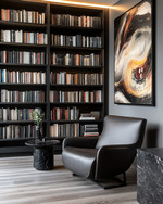 A modern library featuring floor-to-ceiling matte black bookshelves filled with books, a low-profile charcoal leather armchair, a black marble side table, and a large abstract art piece on a wall painted in Benjamin Moore's Gray Owl, with warm task lighting.