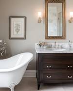 Traditional bathroom featuring a white clawfoot tub, a dark wood console vanity with a Carrara marble top, polished nickel fixtures, and an ornate gilded mirror above the sink, all under warm sconce lighting. — close-up of textures and materials