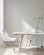 A bright Scandinavian dining room featuring a light birch wood dining table, minimalist white chairs, a simple linen tablecloth, and a clear glass vase with a single green branch, all set against soft grey walls. — alternate angle