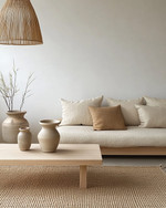 A serene Japandi living room featuring a low-slung sofa in natural linen, a simple light oak coffee table, and a woven jute rug, complemented by a bamboo pendant light and ceramic vases in muted tones. — styling and décor detail