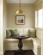 A cozy traditional breakfast nook featuring a built-in cream banquette with sage green cushions, a round dark wood pedestal table, and a classic brass pendant light, all bathed in soft morning light. — close-up of textures and materials