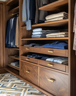 A meticulously organized Mid-Century Modern closet featuring warm walnut built-in shelving, brass pull handles, and open displays of neatly folded garments in an earthy color palette, with a subtle geometric rug.
