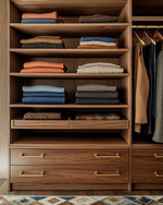 A meticulously organized Mid-Century Modern closet featuring warm walnut built-in shelving, brass pull handles, and open displays of neatly folded garments in an earthy color palette, with a subtle geometric rug. — styling and décor detail