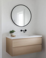 A bright Scandinavian powder room with white walls, a light wood floating vanity, a minimalist round mirror, and a single black wall-mounted faucet, accented by a small green plant. — styling and décor detail
