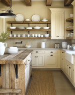 A cozy rustic kitchen featuring creamy off-white cabinets, a reclaimed wood island, and open shelving displaying white stoneware. Wrought iron hardware and a sisal runner add to the warm, inviting atmosphere, with natural light streaming in. — styling and décor detail