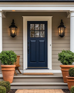 A cozy traditional exterior featuring a warm gray facade with creamy white trim, a deep blue front door, and classic black lantern sconces flanking the entrance. Potted green plants in terracotta pots sit on either side of the door, and a traditional wooden bench offers a welcoming touch. — close-up of textures and materials