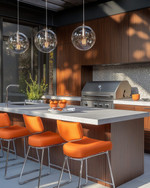 A stylish Mid-Century Modern outdoor kitchen featuring a grey terrazzo countertop, rich walnut-toned cabinetry, and a sleek brushed stainless steel grill. Orange upholstered bar stools with chrome legs sit at the island, under a cluster of spherical globe pendant lights. — alternate angle