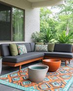 A family-friendly Mid-Century Modern patio featuring a low-profile charcoal grey L-shaped sectional with olive green performance fabric cushions, a geometric outdoor rug in burnt orange and teal, and teak wood accent tables. Large, sculptural ceramic planters with pet-safe plants are arranged around the seating area, with a subtle concrete water bowl for pets integrated into the design. — alternate angle