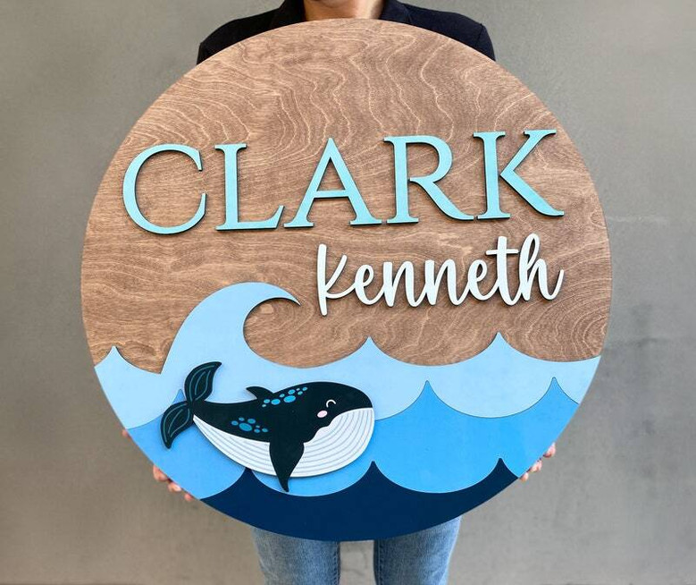 Whale-themed round wood nursery sign personalized with baby name, ocean wall decor plaque, thoughtful baby shower gift